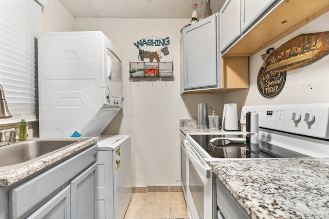 kitchen with a textured ceiling, white electric stove, gray cabinets, and stacked washer / dryer