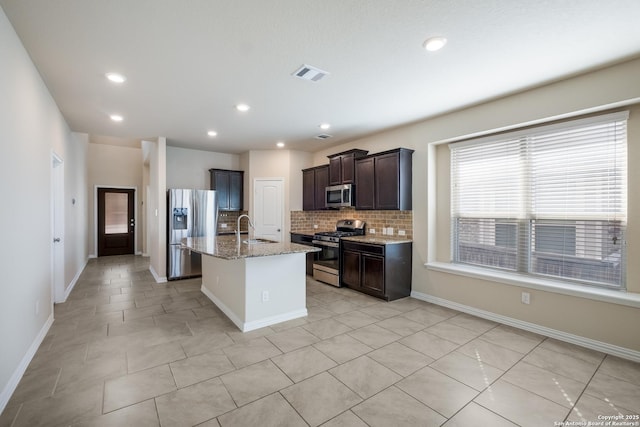 kitchen featuring visible vents, an island with sink, light stone counters, stainless steel appliances, and a sink