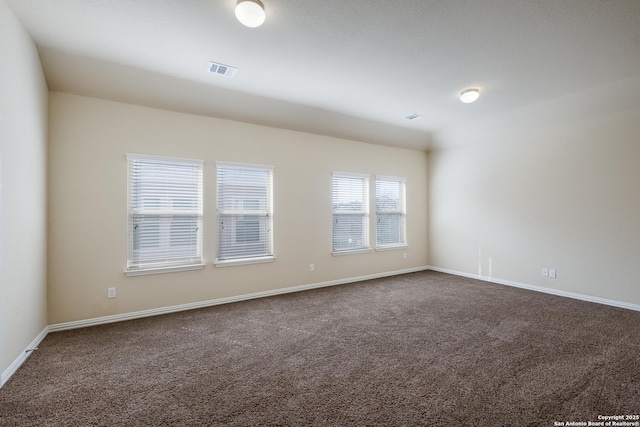 empty room with dark colored carpet, visible vents, and baseboards