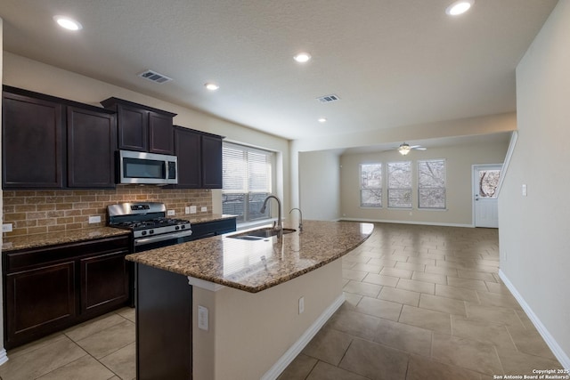 kitchen with stone countertops, a sink, visible vents, appliances with stainless steel finishes, and a center island with sink