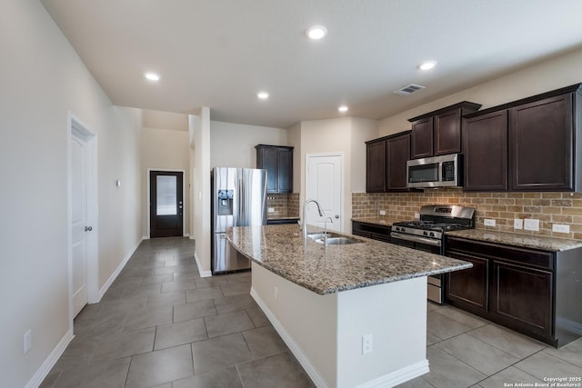 kitchen featuring light stone counters, stainless steel appliances, a sink, visible vents, and an island with sink