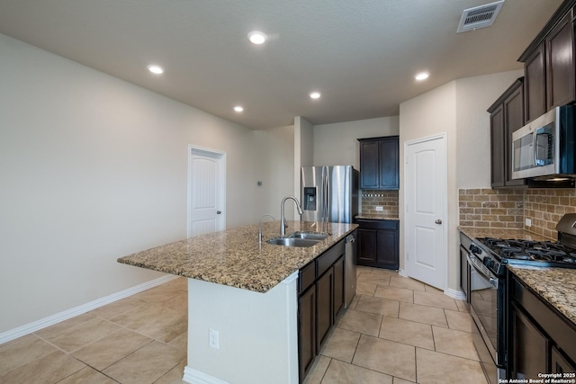 kitchen with a center island with sink, stainless steel appliances, visible vents, a sink, and light stone countertops