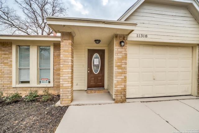 view of exterior entry featuring a garage and brick siding