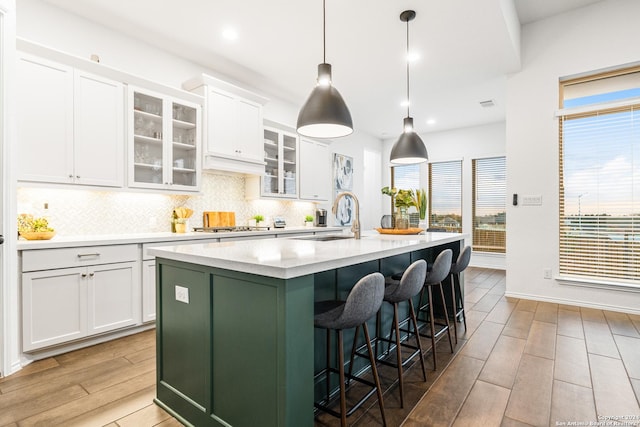 kitchen featuring glass insert cabinets, a kitchen island with sink, white cabinets, and hanging light fixtures