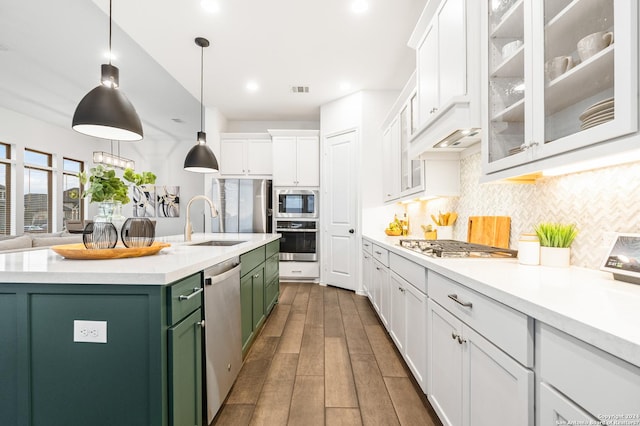 kitchen featuring an island with sink, stainless steel appliances, light countertops, white cabinetry, and green cabinetry