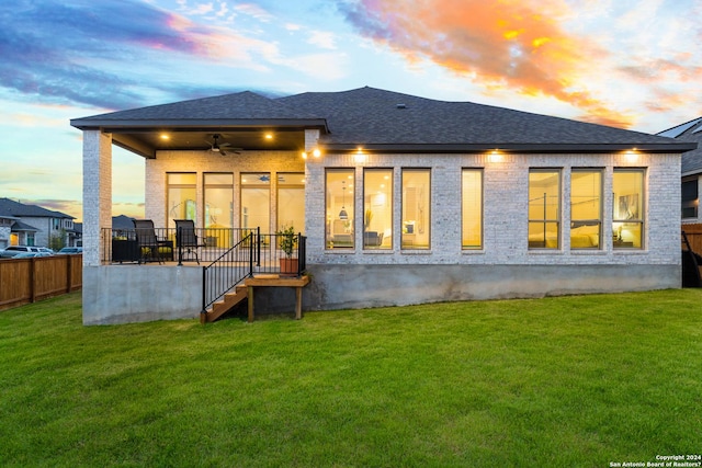 back of property featuring ceiling fan, roof with shingles, a lawn, and fence