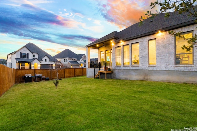 back of house at dusk featuring a fenced backyard and a yard