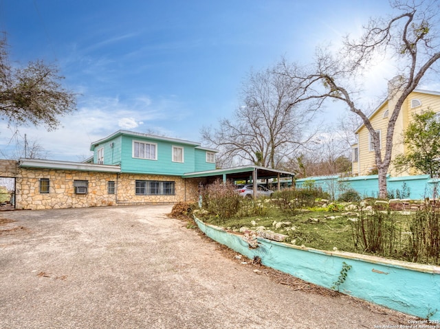 back of property featuring stone siding, driveway, and fence