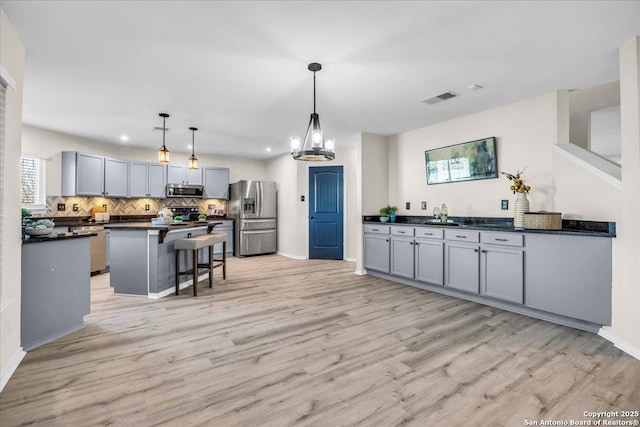 kitchen featuring decorative light fixtures, dark countertops, gray cabinetry, appliances with stainless steel finishes, and a kitchen bar