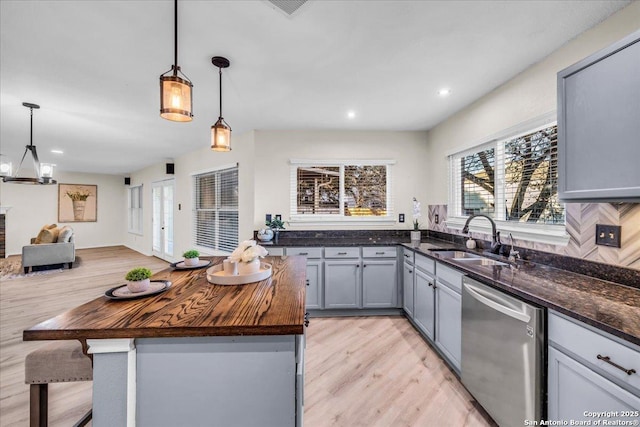 kitchen featuring dishwasher, a kitchen island, decorative light fixtures, wooden counters, and a sink