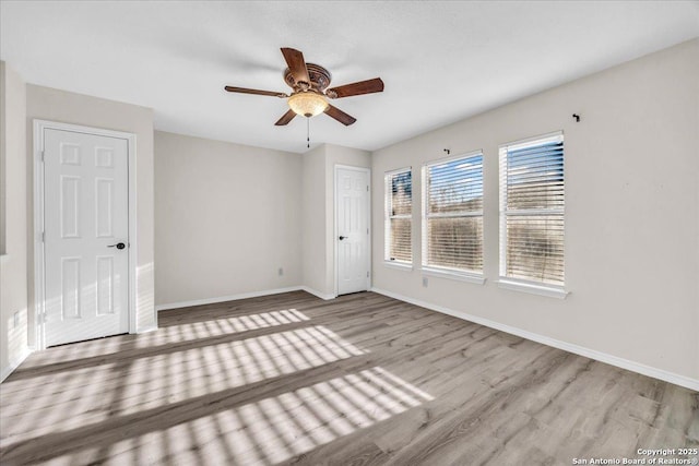 spare room with light wood finished floors, a ceiling fan, and baseboards