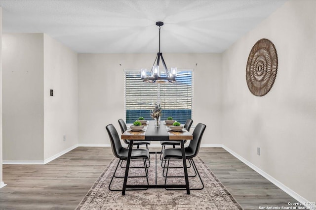 dining space with wood finished floors, a textured ceiling, baseboards, and an inviting chandelier