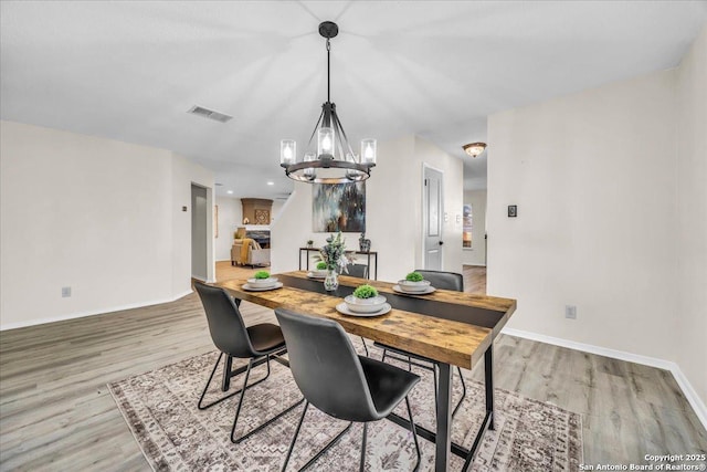 dining area featuring a notable chandelier, light wood-style flooring, visible vents, and baseboards