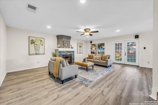 living room with french doors, visible vents, light wood-style floors, a stone fireplace, and baseboards