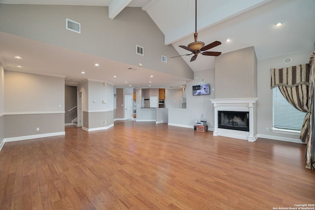 unfurnished living room featuring visible vents, a fireplace with raised hearth, ceiling fan, light wood-type flooring, and beam ceiling