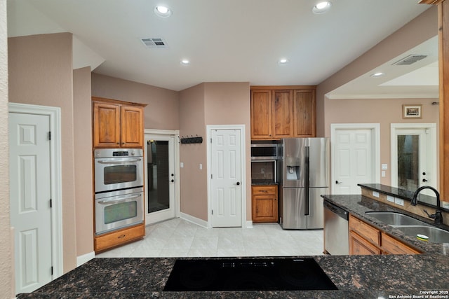 kitchen featuring a sink, visible vents, appliances with stainless steel finishes, dark stone counters, and brown cabinetry