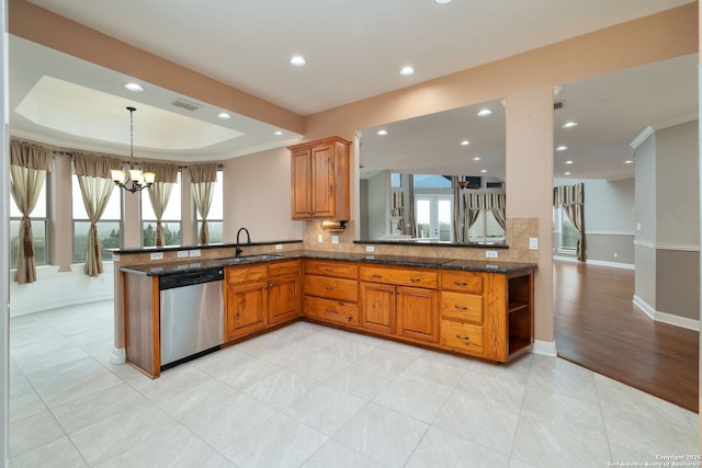 kitchen with brown cabinetry, a raised ceiling, a peninsula, stainless steel dishwasher, and a sink