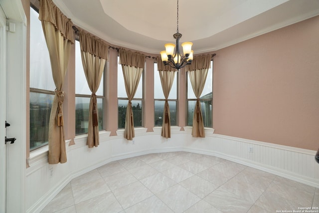 unfurnished dining area with tile patterned flooring, a notable chandelier, a wainscoted wall, ornamental molding, and a raised ceiling