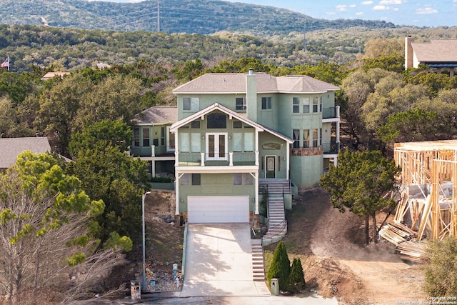 view of front facade featuring driveway, a garage, stairs, french doors, and a wooded view