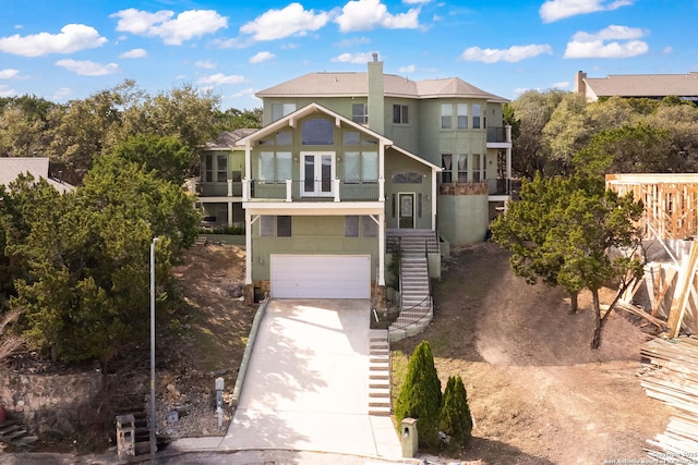 view of front of home featuring a garage, a chimney, concrete driveway, and a balcony