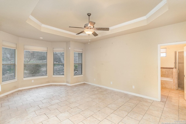 empty room featuring ornamental molding, a tray ceiling, plenty of natural light, and light tile patterned floors