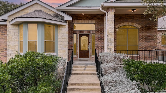 doorway to property with brick siding and a shingled roof