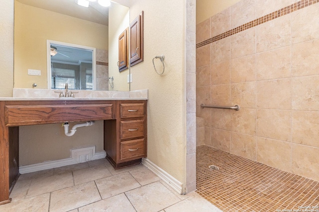 full bath with a tile shower, vanity, baseboards, and stone tile floors