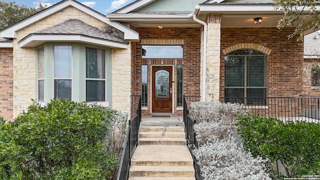 entrance to property featuring a shingled roof and brick siding