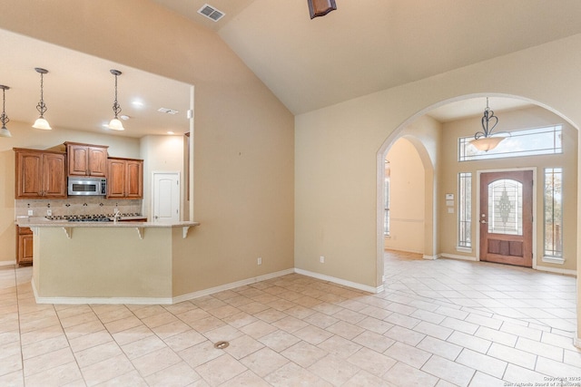 foyer entrance with arched walkways, light tile patterned floors, visible vents, high vaulted ceiling, and baseboards