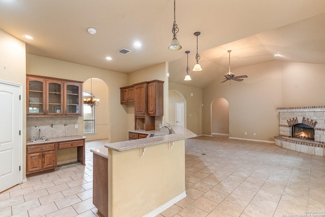 kitchen with arched walkways, a fireplace, a sink, brown cabinets, and glass insert cabinets