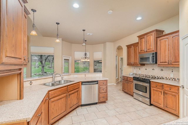 kitchen with tasteful backsplash, brown cabinets, decorative light fixtures, stainless steel appliances, and a sink