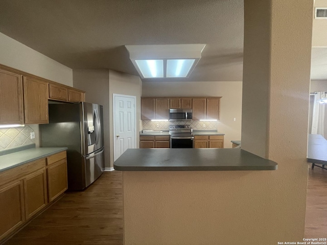 kitchen with appliances with stainless steel finishes, dark wood-type flooring, and tasteful backsplash