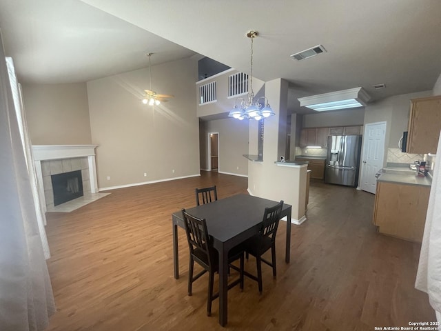 dining space with baseboards, visible vents, a tile fireplace, wood finished floors, and ceiling fan with notable chandelier