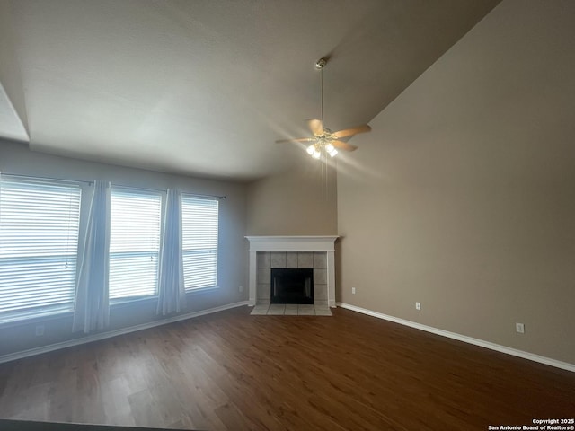 unfurnished living room with baseboards, a ceiling fan, a tiled fireplace, dark wood-style floors, and vaulted ceiling