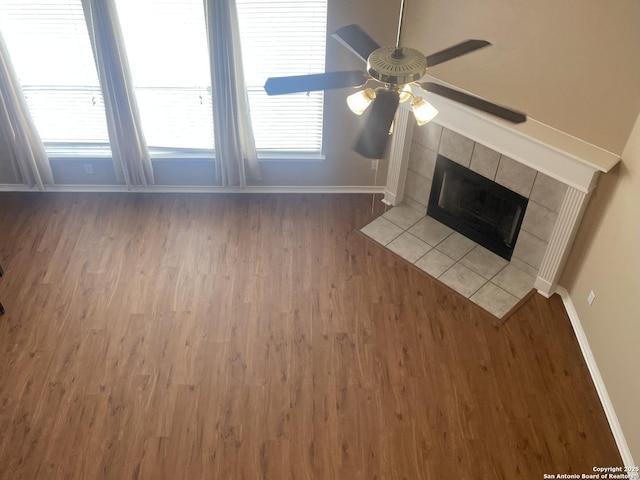 unfurnished living room featuring a healthy amount of sunlight, baseboards, a tiled fireplace, and wood finished floors