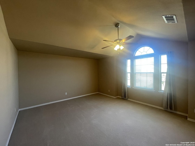 carpeted spare room featuring a ceiling fan, visible vents, vaulted ceiling, and baseboards