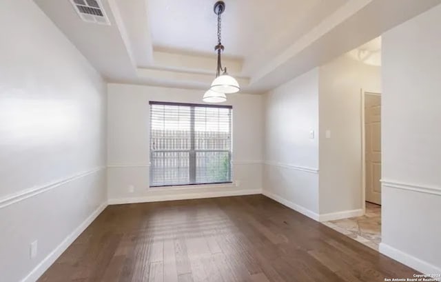 spare room featuring a raised ceiling, visible vents, baseboards, and wood finished floors