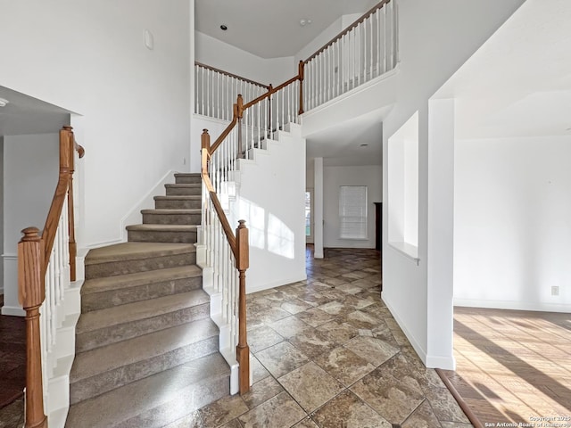 stairs with a towering ceiling, stone finish flooring, and baseboards