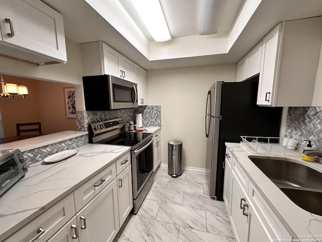 kitchen with light stone counters, marble finish floor, stainless steel appliances, white cabinetry, and a sink