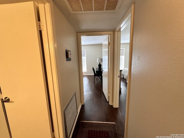 corridor with a textured wall, dark wood-type flooring, visible vents, and baseboards