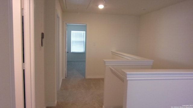 hall featuring attic access, light colored carpet, and baseboards