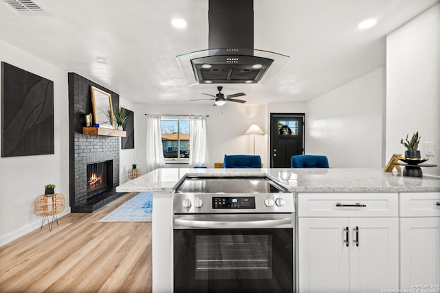 kitchen featuring light stone counters, electric range, white cabinetry, and island range hood