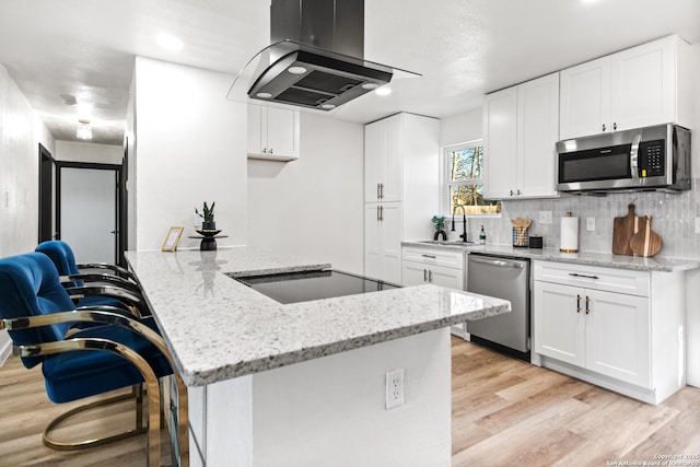 kitchen with island exhaust hood, white cabinetry, stainless steel appliances, and a breakfast bar area