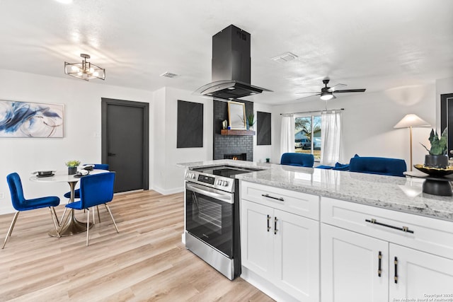 kitchen with light stone counters, island exhaust hood, stainless steel electric stove, open floor plan, and white cabinets