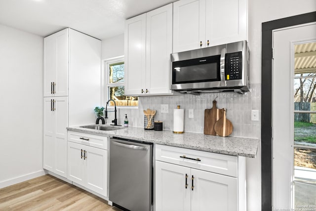 kitchen featuring light stone counters, stainless steel appliances, a sink, white cabinets, and tasteful backsplash