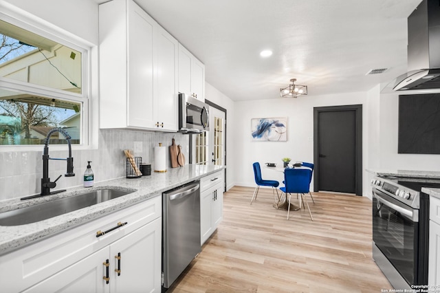 kitchen with light stone counters, island exhaust hood, appliances with stainless steel finishes, white cabinetry, and a sink