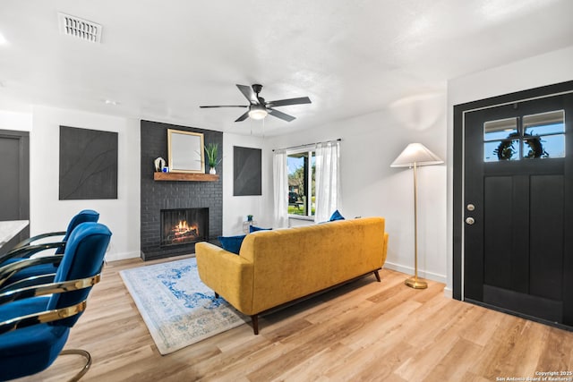 living room featuring light wood-style flooring, a fireplace, a ceiling fan, visible vents, and baseboards