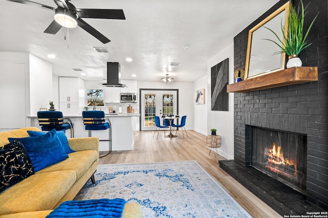 living room with french doors, visible vents, light wood-style flooring, a brick fireplace, and baseboards