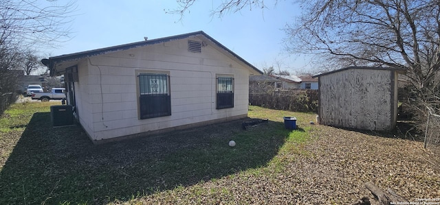 view of side of home featuring an outbuilding, central AC, a storage unit, and fence