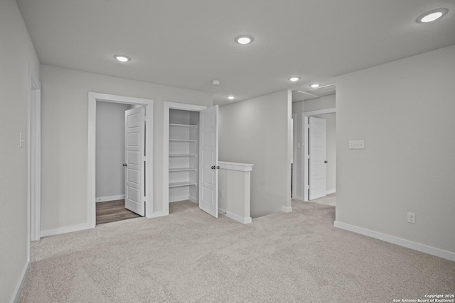 unfurnished bedroom featuring carpet, recessed lighting, a walk in closet, baseboards, and a closet